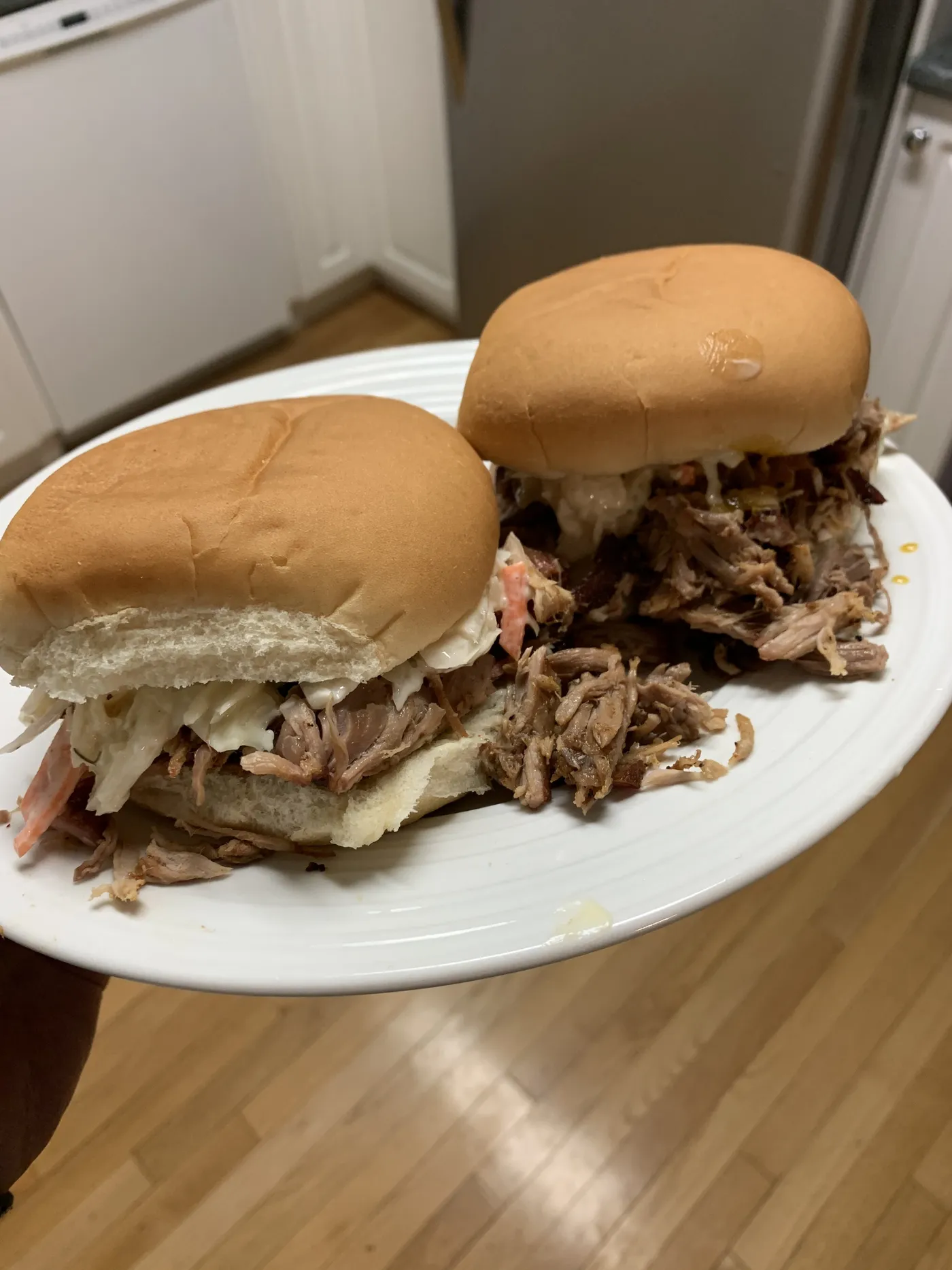 Two pulled pork sandwiches on soft white buns with creamy coleslaw, on a white plate