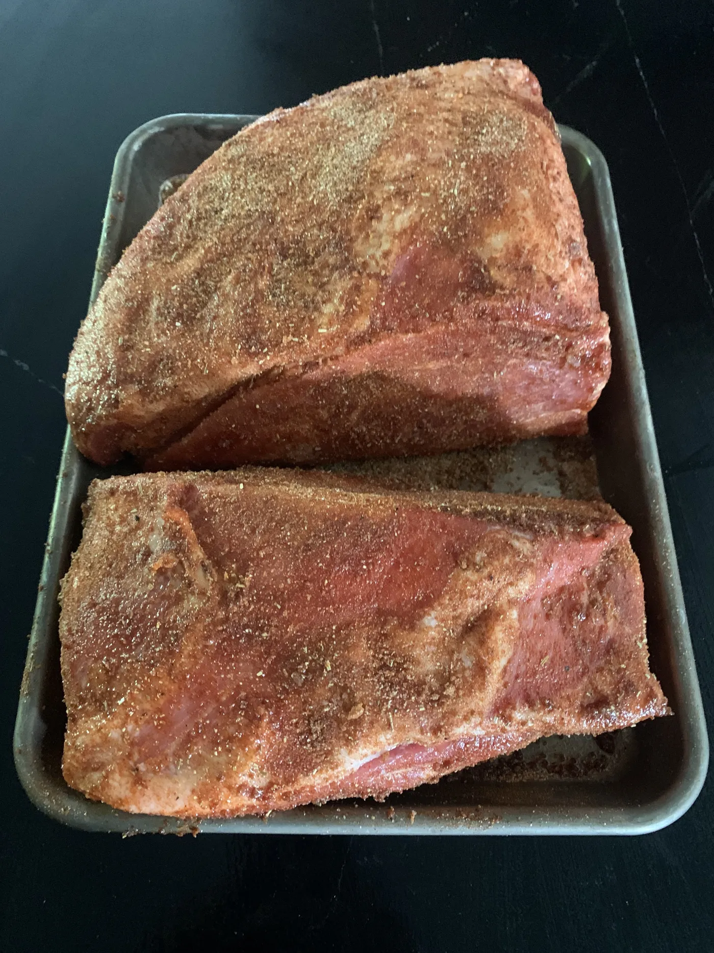 The two pork butt halves coated in Memphis Dust on the sheet pan