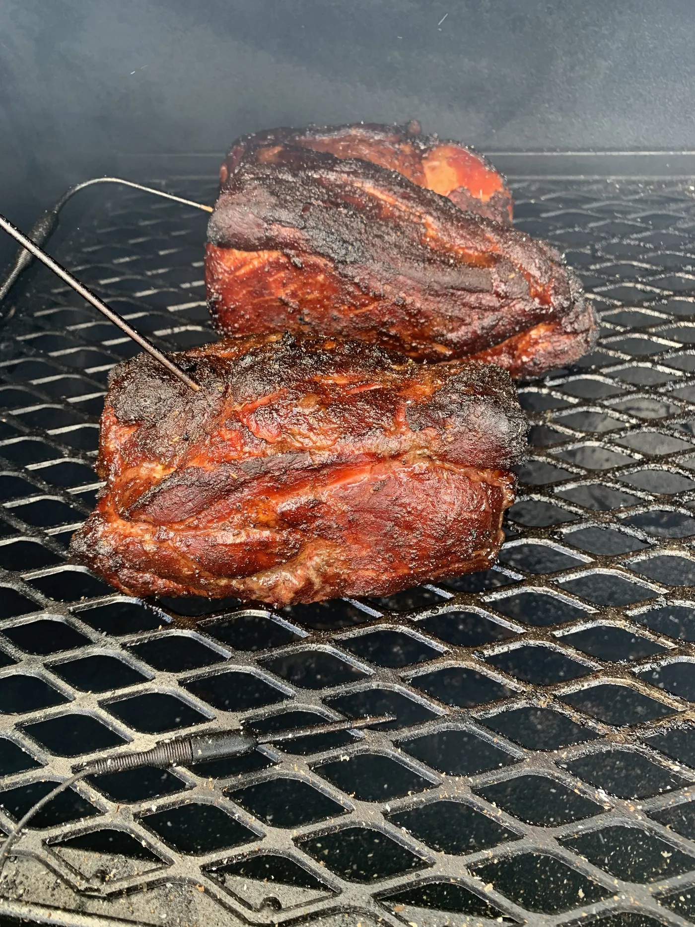 Both halves of the pork butt on the offset grate four and a half hours in, the rub turning dark red, with a probe wire in the front piece