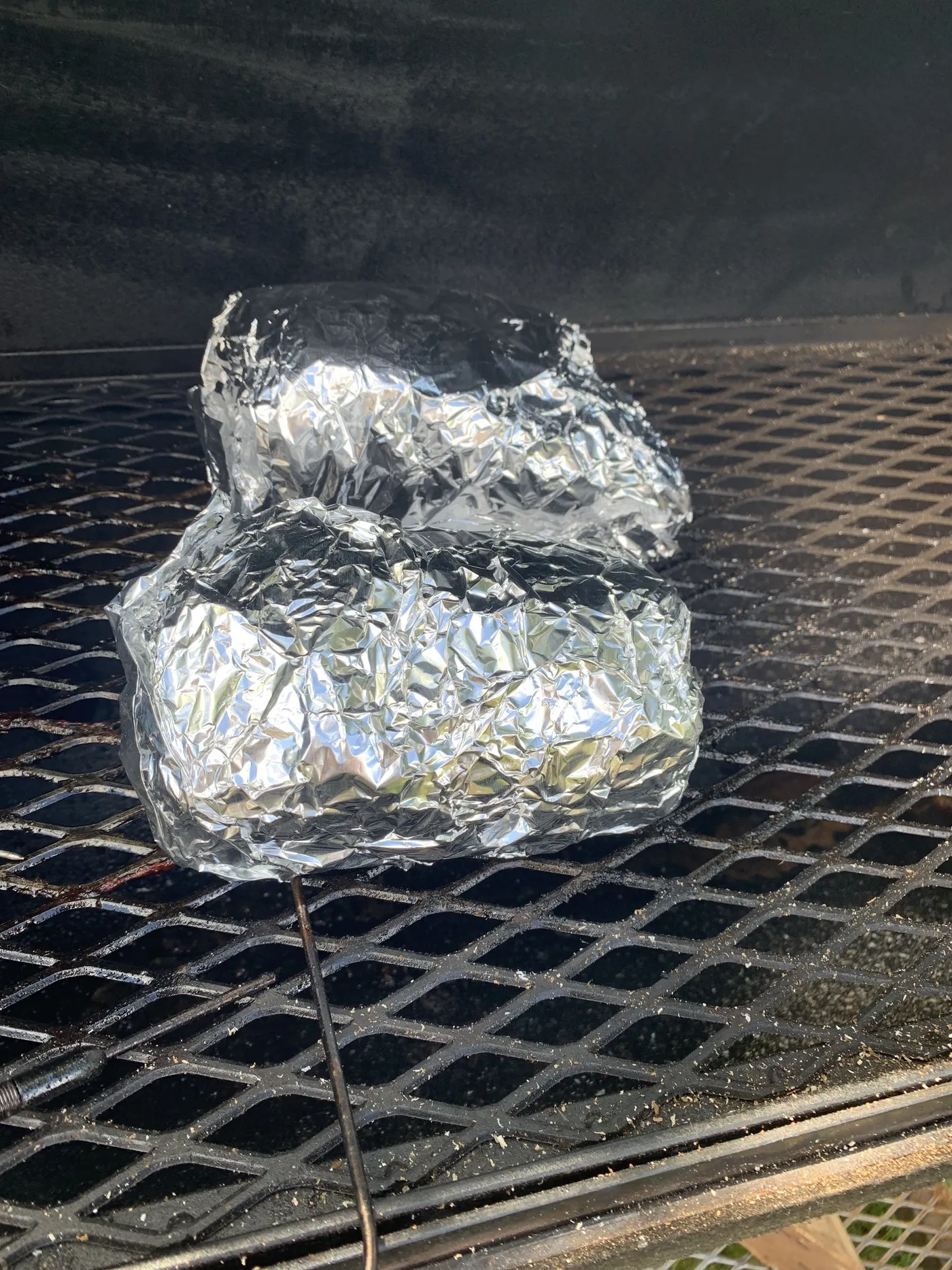 Both pork butt halves wrapped in foil on the offset grate, a probe wire running out of the front one
